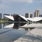 Danielle Art Original Acrylic and Oil Paintings Chengdu architecture: Modern building reflected in water, city skyline in background.