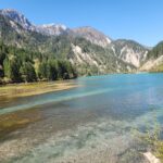 Danielle Art Original Acrylic and Oil Paintings Jiuzhaigou's stunning turquoise lake surrounded by lush green mountains and forests under a clear blue sky.