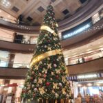 Danielle Art Original Acrylic and Oil Paintings Large Christmas tree inside a shopping mall with Dolce & Gabbana store in background.