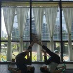 Danielle Art Original Acrylic and Oil Paintings Two women doing partner yoga in a studio, legs raised and touching, using yoga wheels.