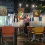 Danielle Art Original Acrylic and Oil Paintings Two women at the "Art Over Coffee Exhibition" surrounded by animal artwork and cafe seating.