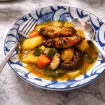 Stew with chicken wings, potatoes, carrots and mushrooms in blue bowl.