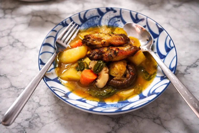 Stew with chicken wings, potatoes, carrots and mushrooms in blue bowl.