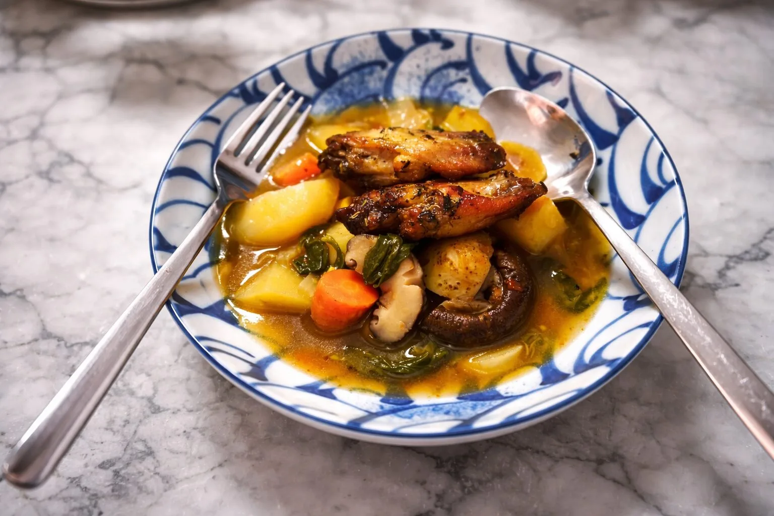Stew with chicken wings, potatoes, carrots and mushrooms in blue bowl.