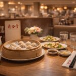 Din Tai Fung meal: soup dumplings, greens, tea, and drinks on a table.