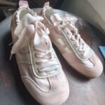 Pair of pink sneakers with ribbon laces on a wooden surface.