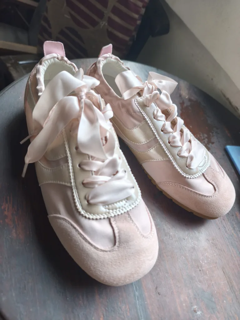 Pair of pink sneakers with ribbon laces on a wooden surface.