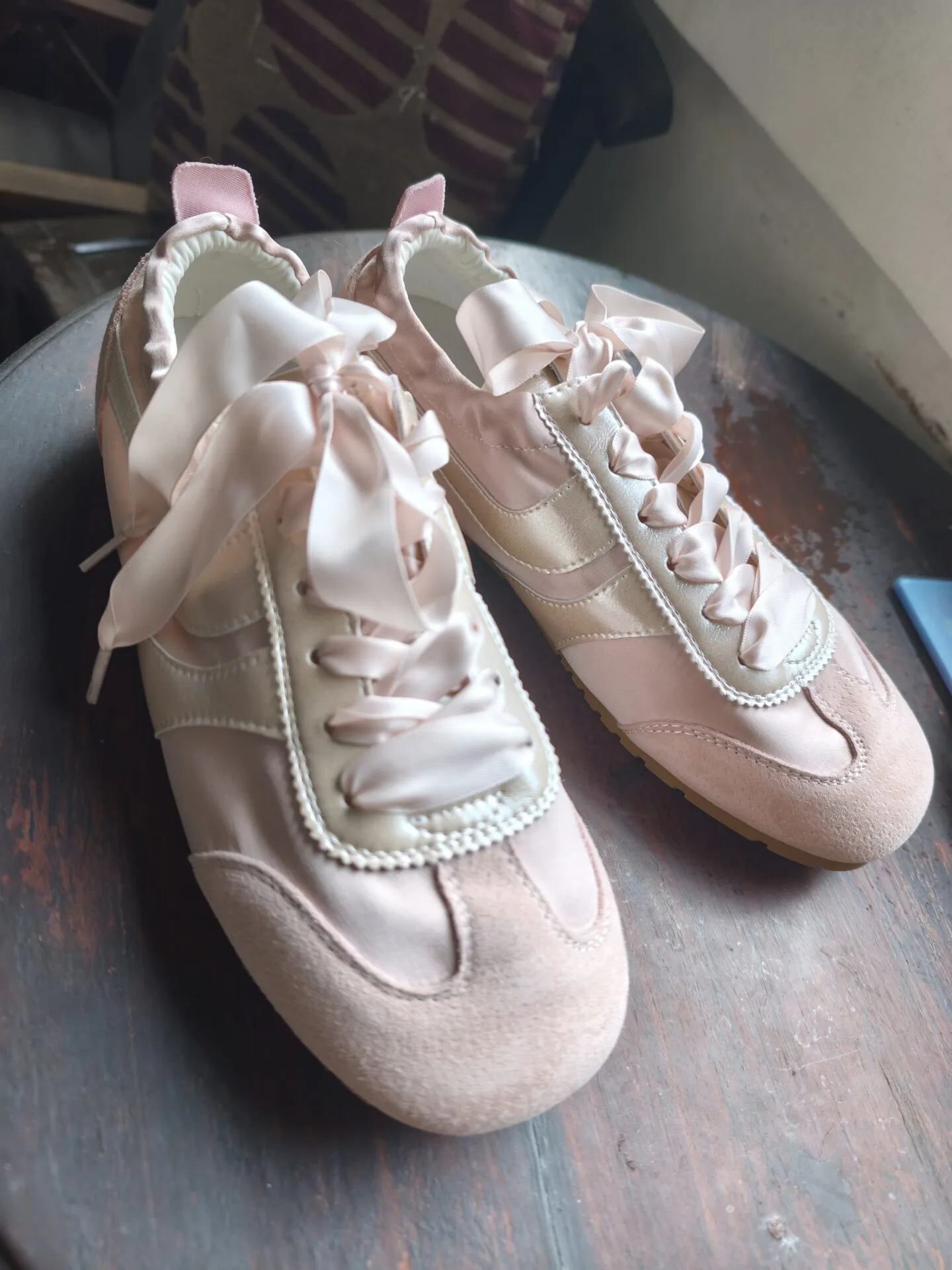 Pair of pink sneakers with ribbon laces on a wooden surface.