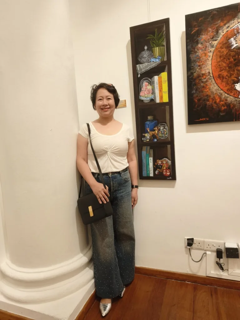 Woman at Splendour of Clementi Artists exhibition, posing near artwork.